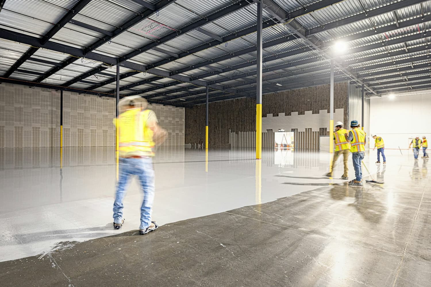 Workers applying a light gray epoxy coating in a large warehouse space