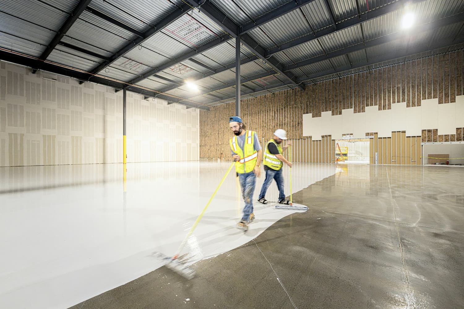 Workers squeegeeing a white epoxy coating across a large warehouse floor